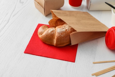 Paper bag with pastry and takeaway food on wooden table