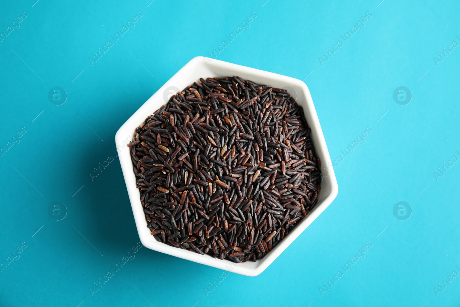 Photo of Bowl with uncooked black rice on color background, top view