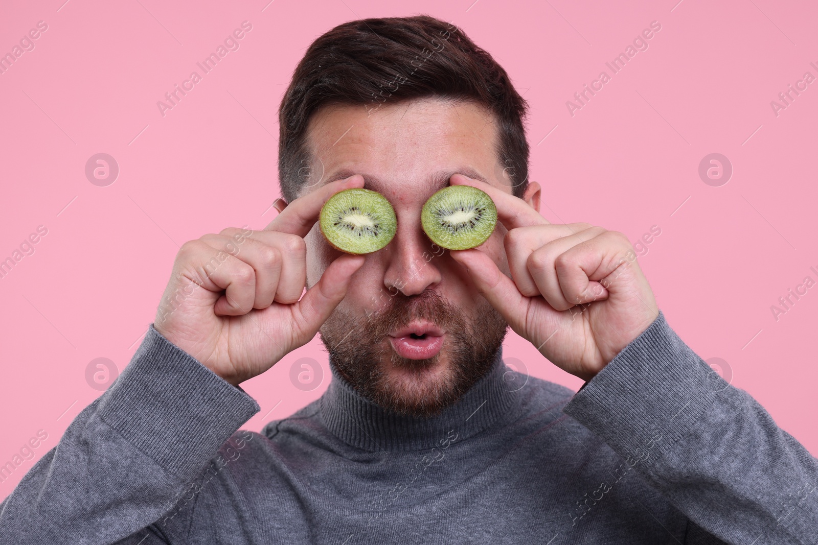 Photo of Man covering his eyes with halves of kiwi on pink background