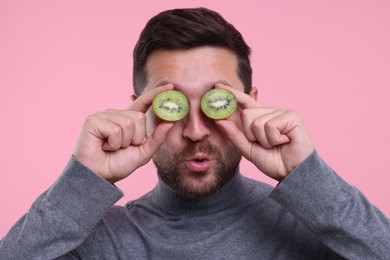 Photo of Man covering his eyes with halves of kiwi on pink background