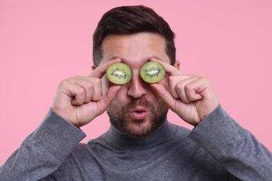 Man covering his eyes with halves of kiwi on pink background