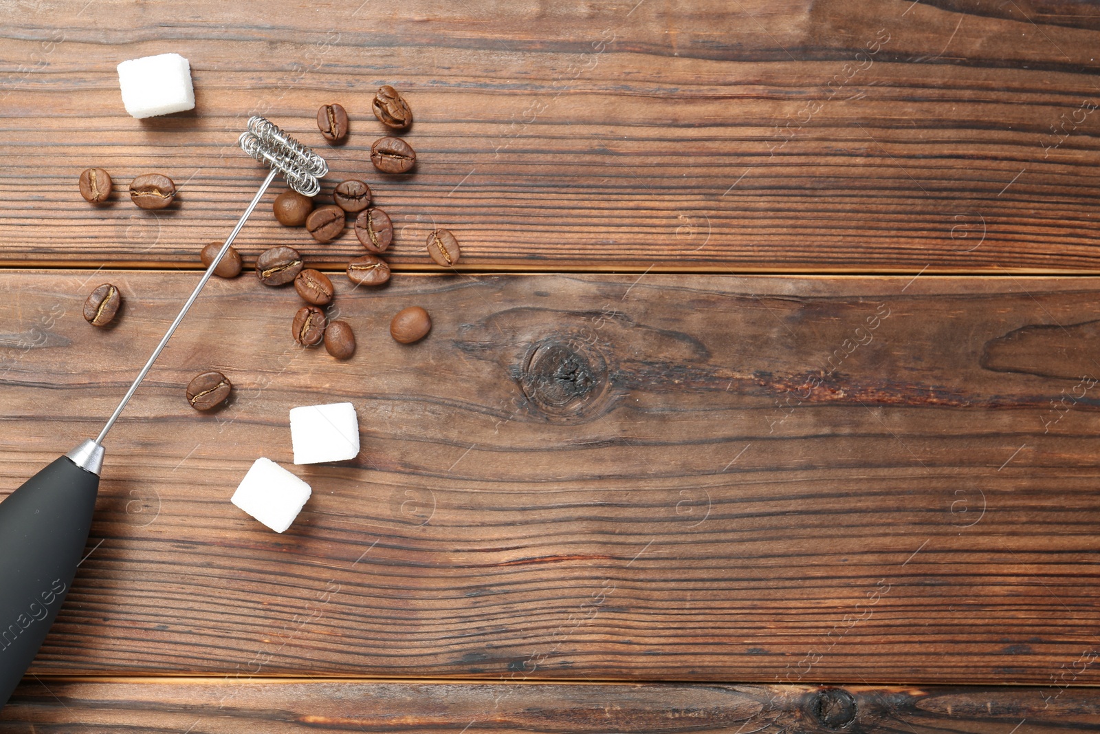 Photo of Black milk frother wand, sugar cubes and coffee beans on wooden table, flat lay. Space for text