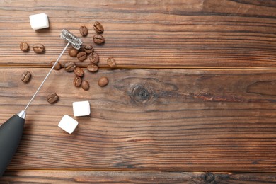 Photo of Black milk frother wand, sugar cubes and coffee beans on wooden table, flat lay. Space for text