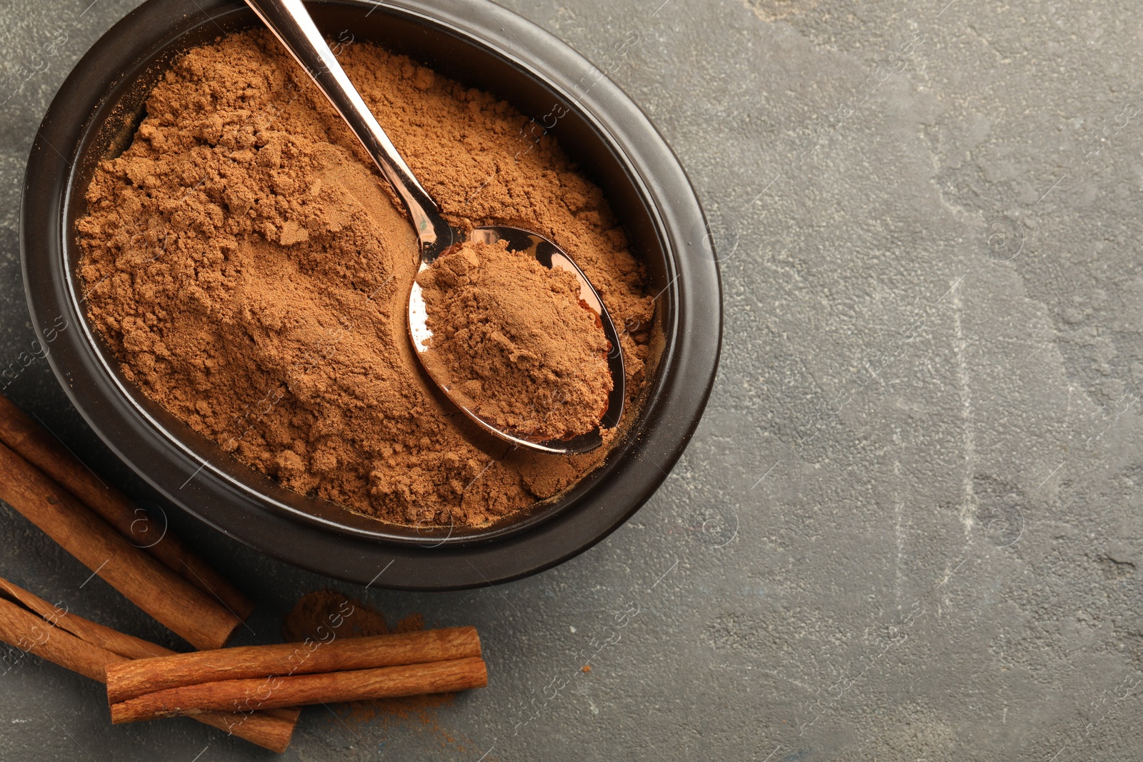 Photo of Bowl of cinnamon powder and sticks on grey table, flat lay. Space for text