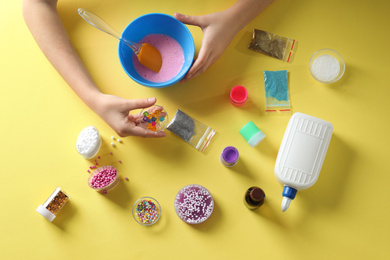 Little girl making slime toy on yellow background, top view