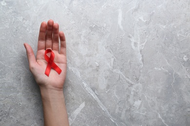 Woman holding red awareness ribbon at light grey marble table, top view with space for text. World AIDS disease day