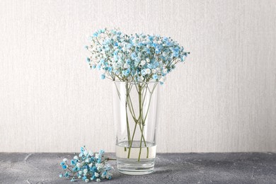 Beautiful gypsophila flowers in vase on grey textured table against light wall