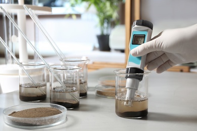 Scientist measuring acidity and pH of soil at table, closeup. Laboratory analysis