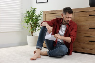 Photo of Sad man ripping photo on floor indoors, space for text. Divorce concept