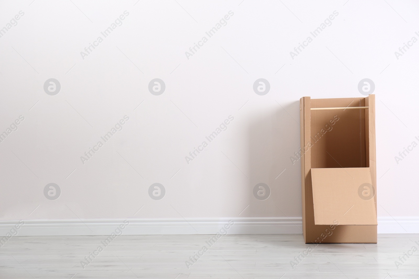 Photo of Cardboard wardrobe box against light wall indoors. Space for text