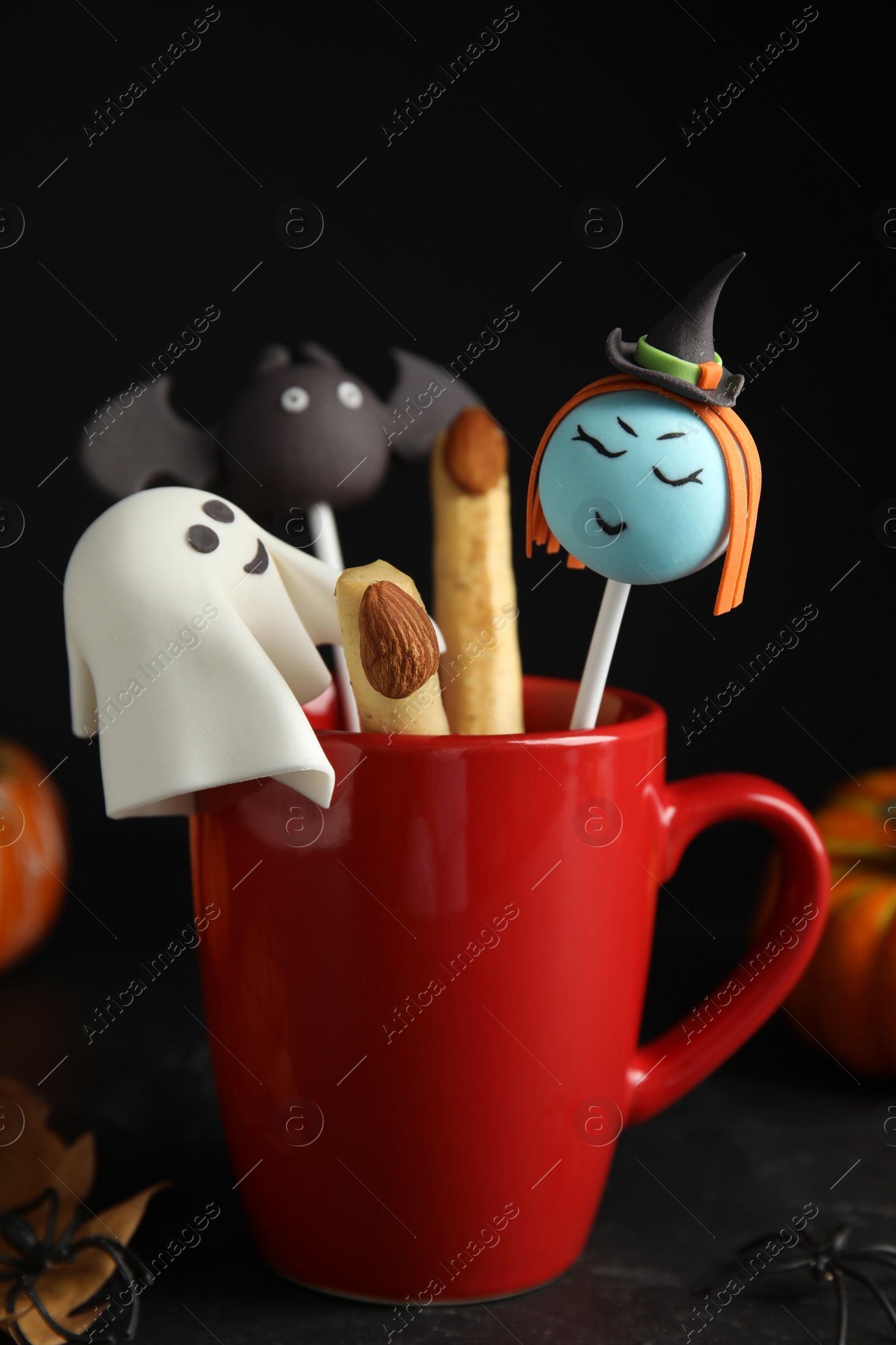 Photo of Different cake pops in cup decorated as monsters on black table. Halloween treat