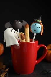 Photo of Different cake pops in cup decorated as monsters on black table. Halloween treat