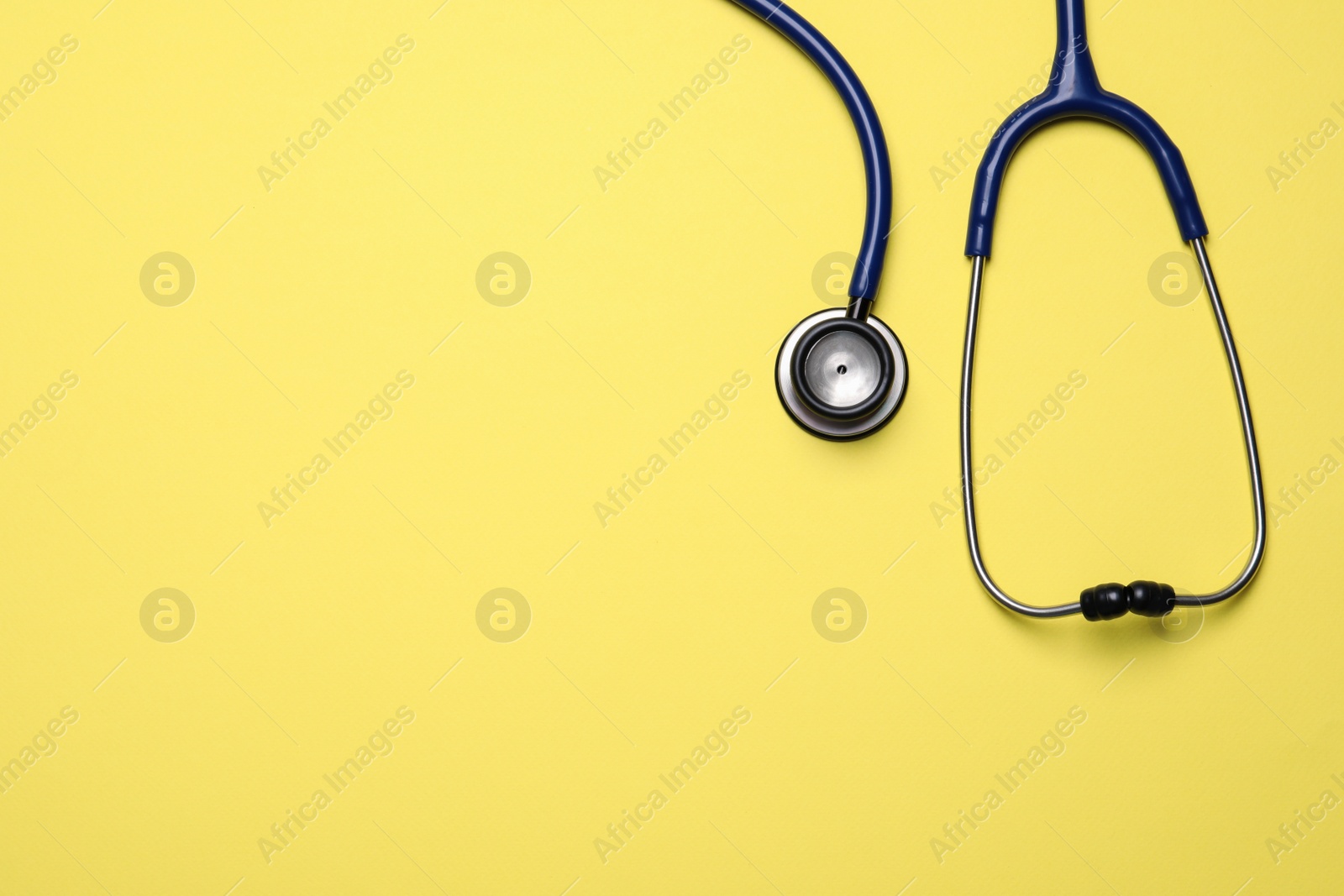 Photo of Stethoscope on yellow background, top view. Space for text