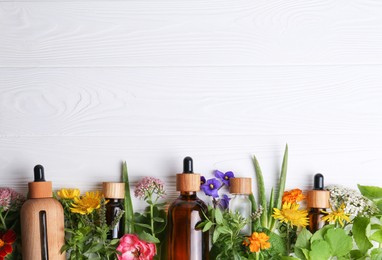 Photo of Glass bottles of aromatic essential oil and different wildflowers on white wooden table, flat lay. Space for text