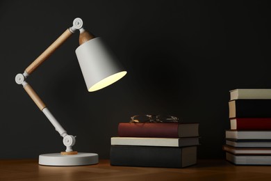 Many books stacked on wooden table near black wall