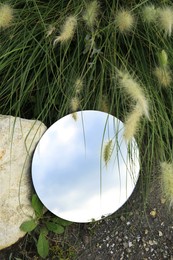 Photo of Round mirror on ground near grass and spikelets reflecting light blue sky