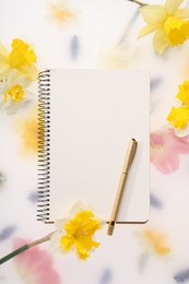 Photo of Guest list. Notebook, pen and daffodils on spring floral background, flat lay