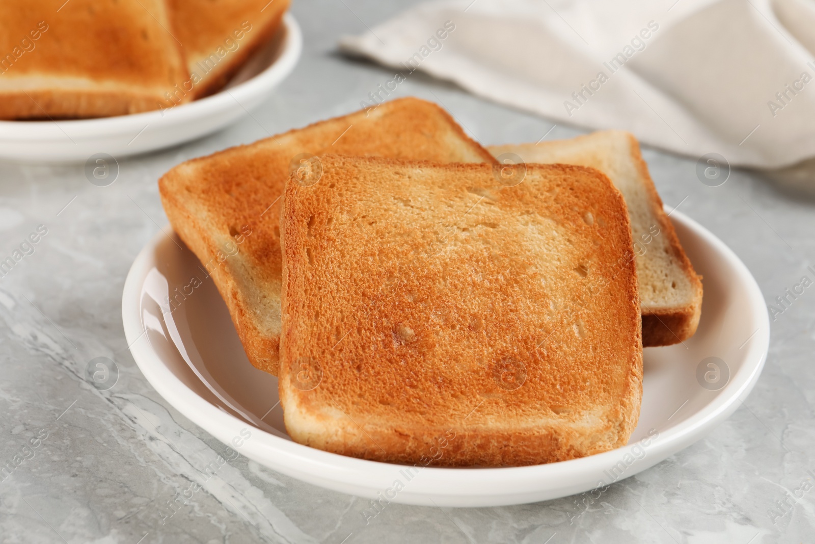 Photo of Plate with slices of delicious toasted bread on gray marble table, closeup