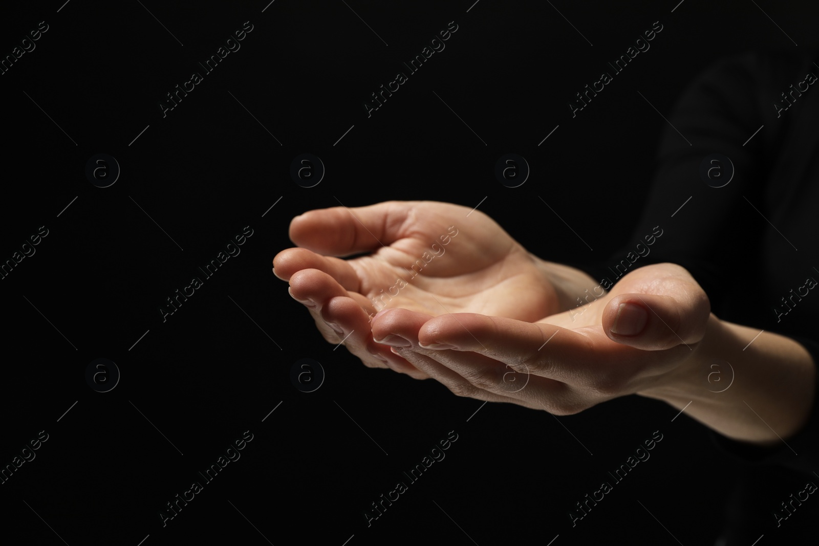 Photo of Religion. Woman with open palms praying on black background, closeup. Space for text