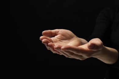 Religion. Woman with open palms praying on black background, closeup. Space for text