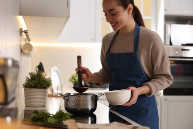 Smiling woman pouring tasty soup into bowl at countertop in kitchen, closeup