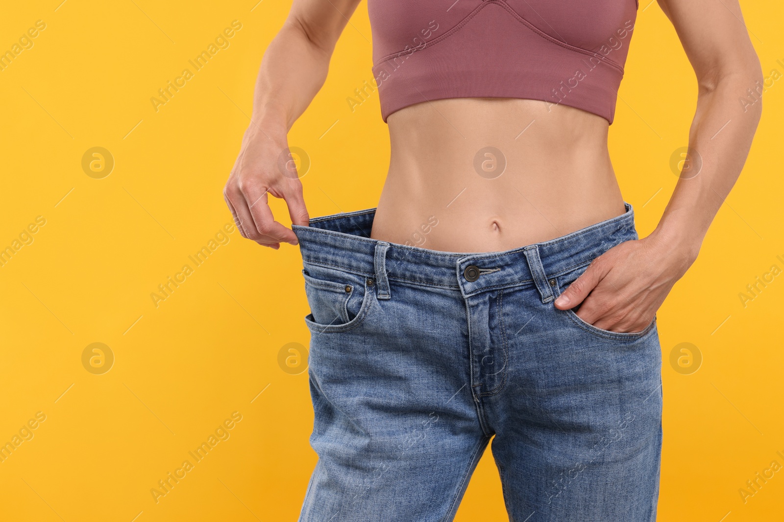 Photo of Slim woman wearing big jeans on yellow background, closeup. Weight loss