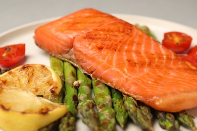 Photo of Tasty grilled salmon with asparagus, tomatoes and lemon on plate, closeup