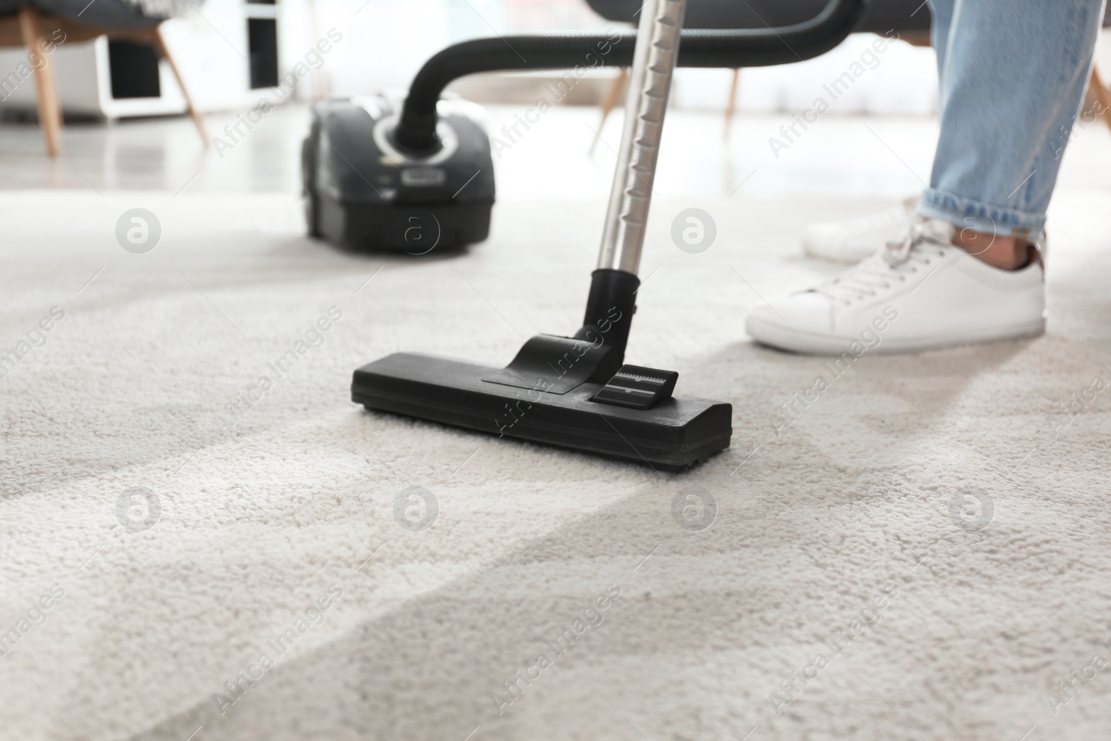 Photo of Janitor hoovering carpet with vacuum cleaner indoors, closeup