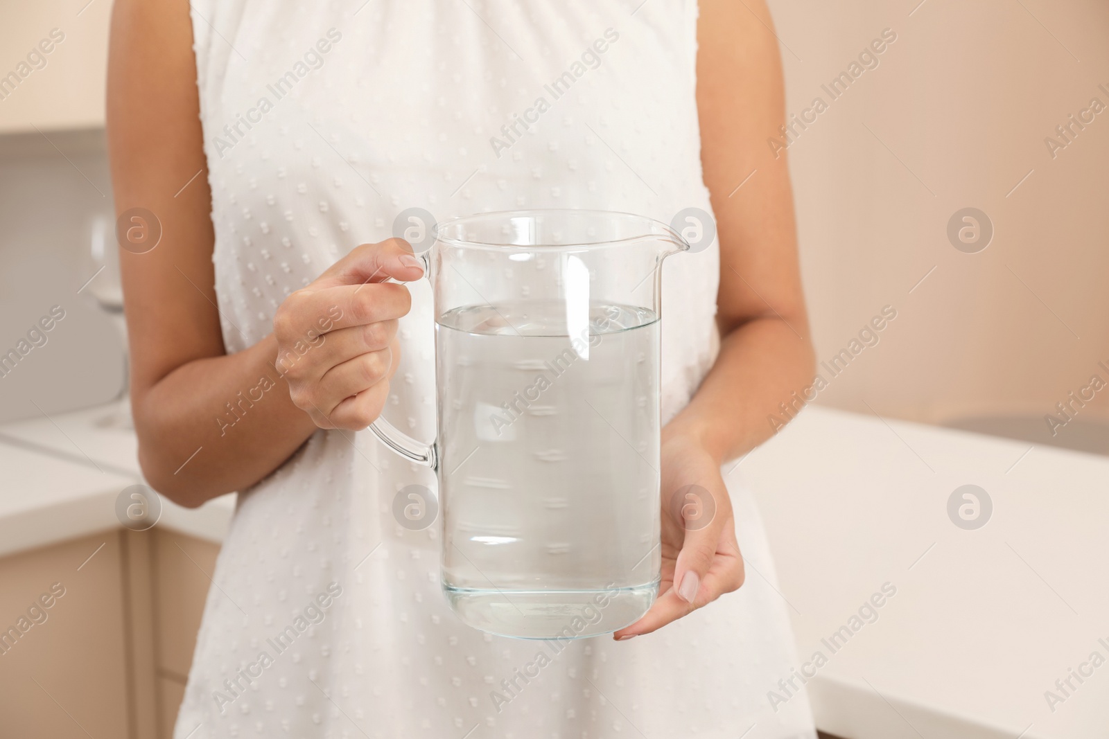 Photo of Woman holding glass jug with water in kitchen, closeup