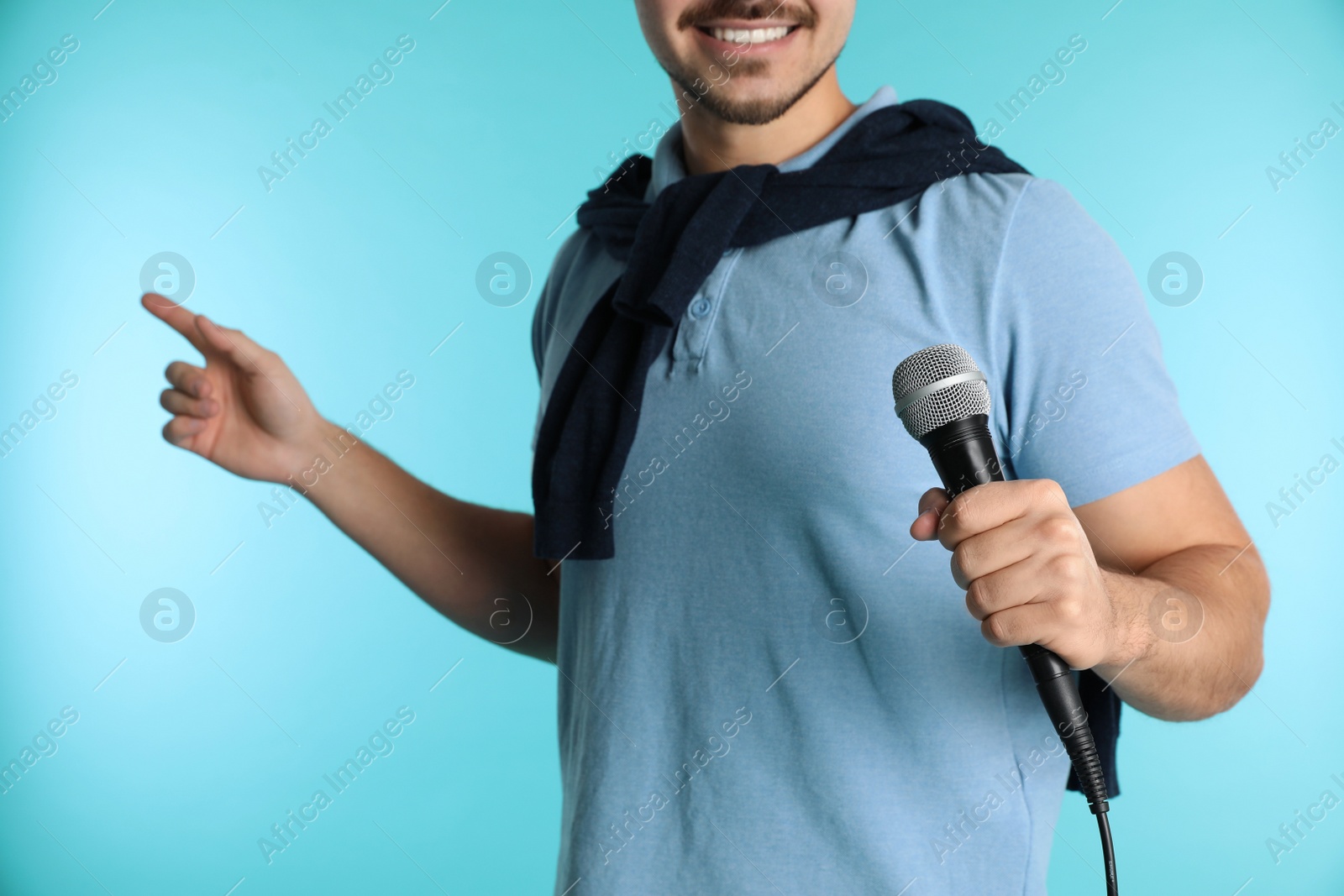 Photo of Young handsome man in casual clothes holding microphone on color background, closeup