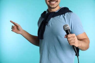 Photo of Young handsome man in casual clothes holding microphone on color background, closeup