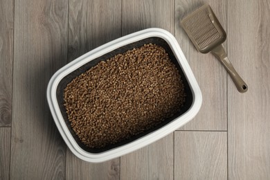 Cat tray with biodegradable litter and scoop on wooden floor, top view