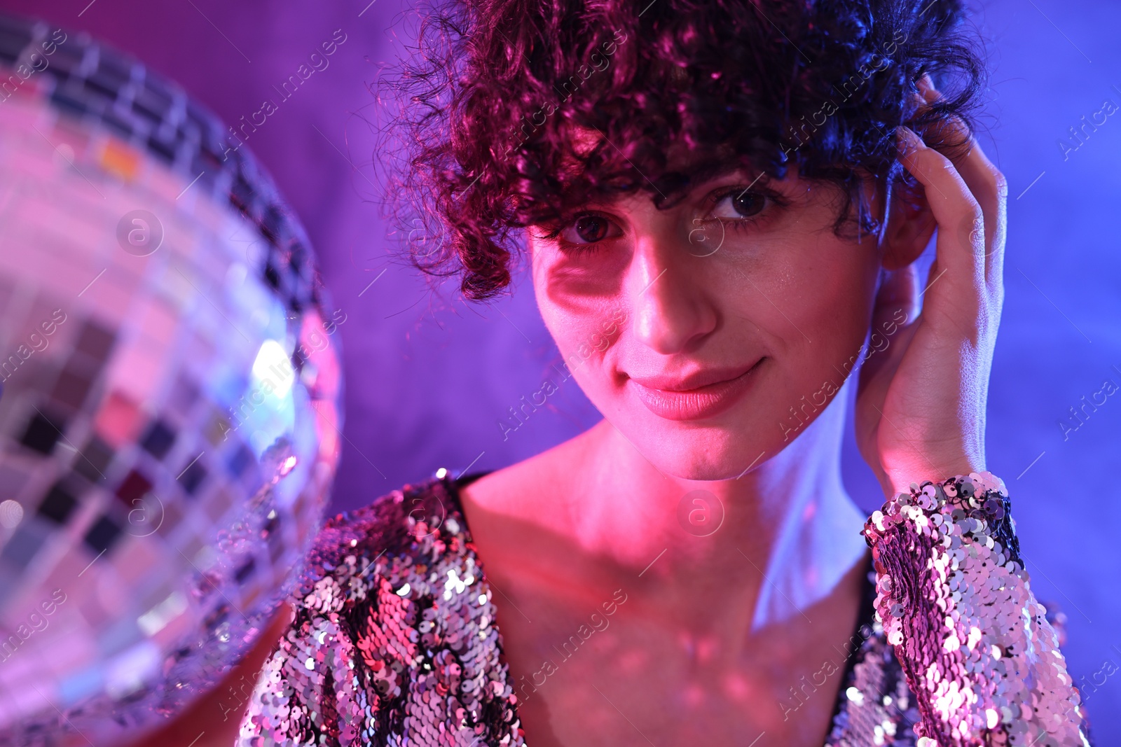 Photo of Beautiful young woman with disco ball posing on color background in neon lights