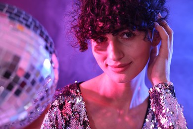 Photo of Beautiful young woman with disco ball posing on color background in neon lights