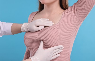 Mammologist checking woman's breast on light blue background, closeup