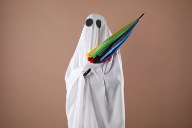 Photo of Person in ghost costume with rainbow umbrella on dark beige background