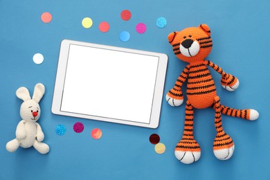 Photo of Modern tablet, confetti and stuffed animals on blue background, flat lay. Space for text
