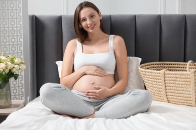 Beautiful pregnant woman sitting on bed indoors