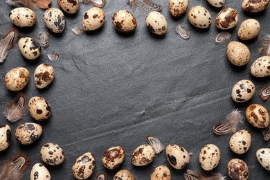 Photo of Frame of quail eggs feathers on black table. Space for text