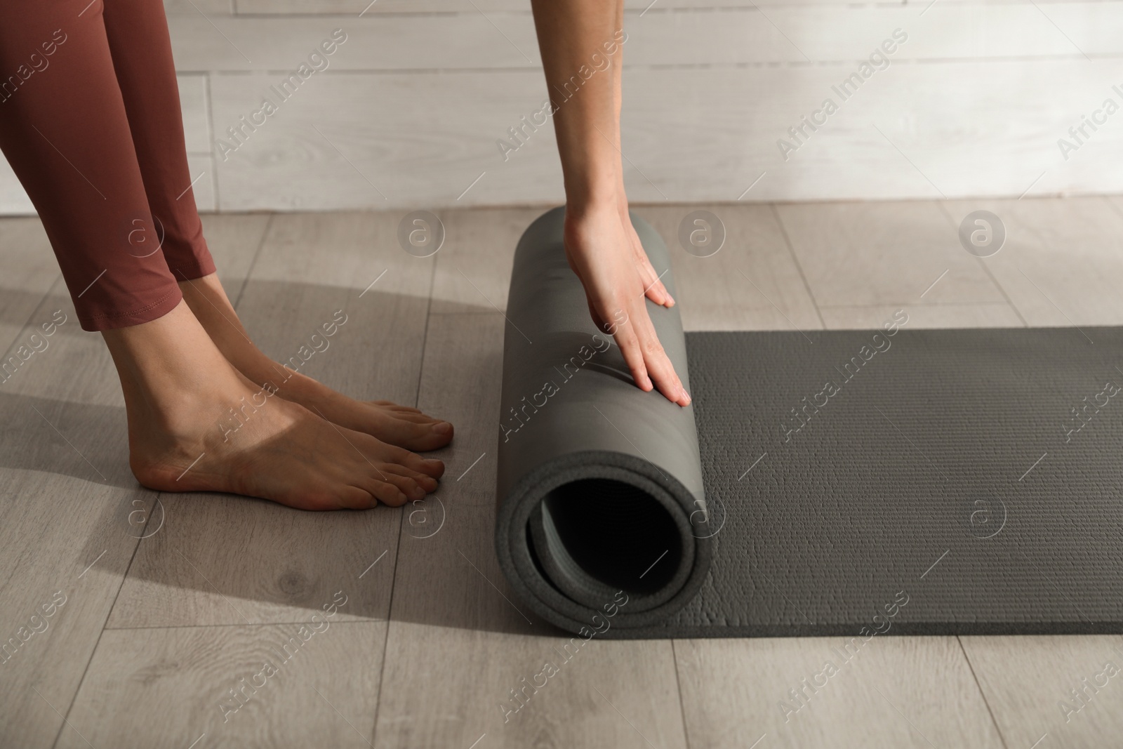 Photo of Woman rolling black yoga mat on floor indoors, closeup