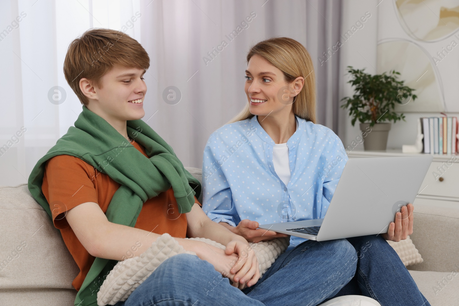 Photo of Happy teenage son and his mother with laptop at home