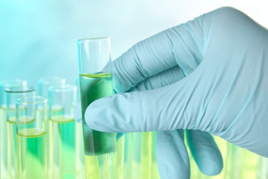 Photo of Scientist taking test tube with liquid sample on color background, closeup