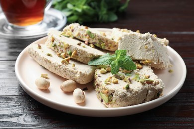 Photo of Pieces of tasty halva with pistachios and mint on wooden table, closeup