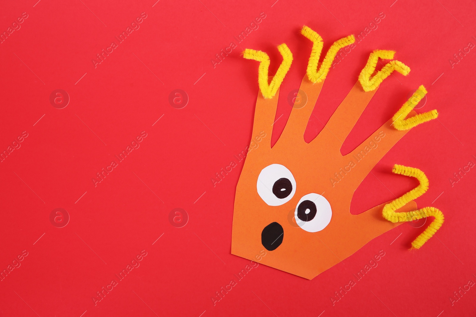 Photo of Funny orange hand shaped monster on red background, top view with space for text. Halloween decoration