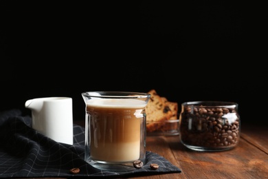 Photo of Composition with glass of delicious coffee drink on wooden table against black background. Space for text