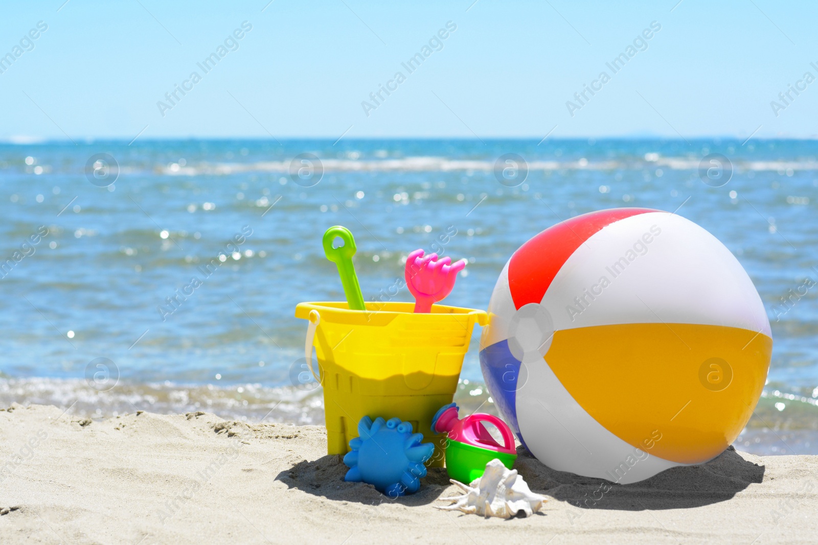 Photo of Set of plastic beach toys and inflatable ball on sand near sea. Space for text