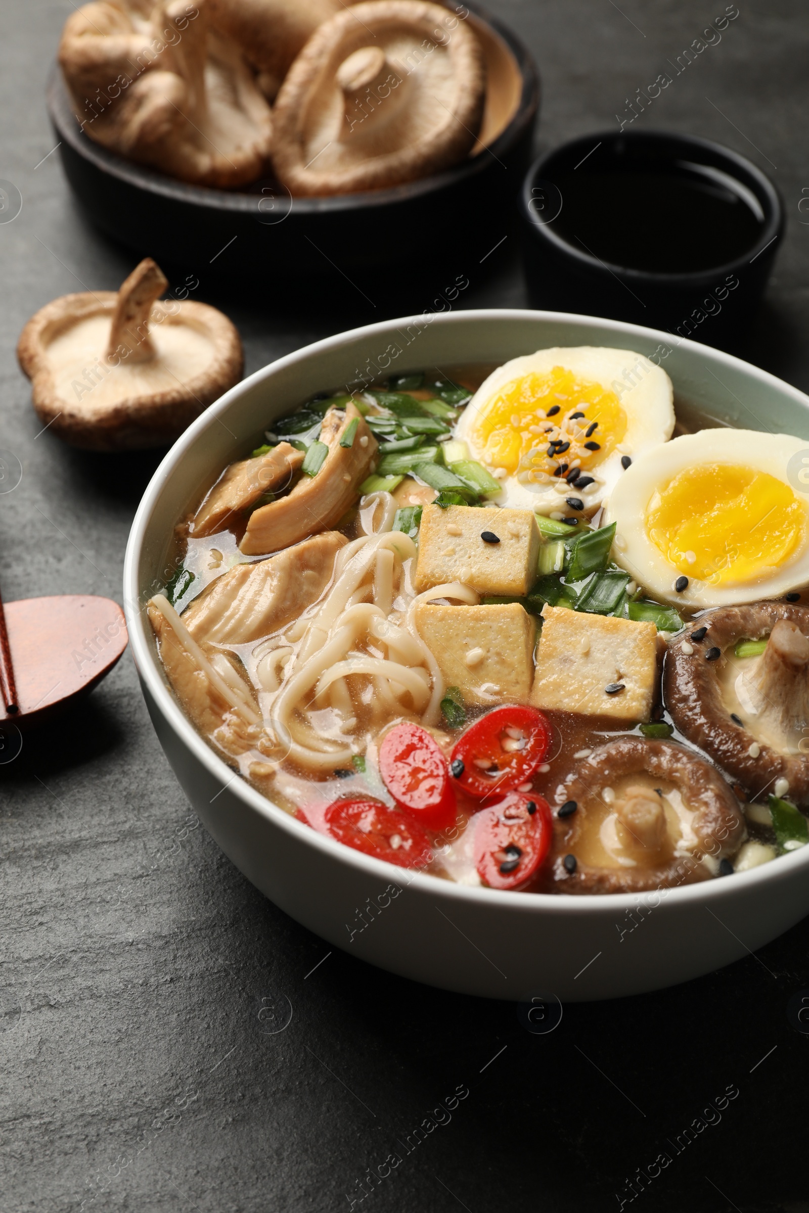 Photo of Noodle soup. Bowl of delicious ramen and ingredients on black table, closeup