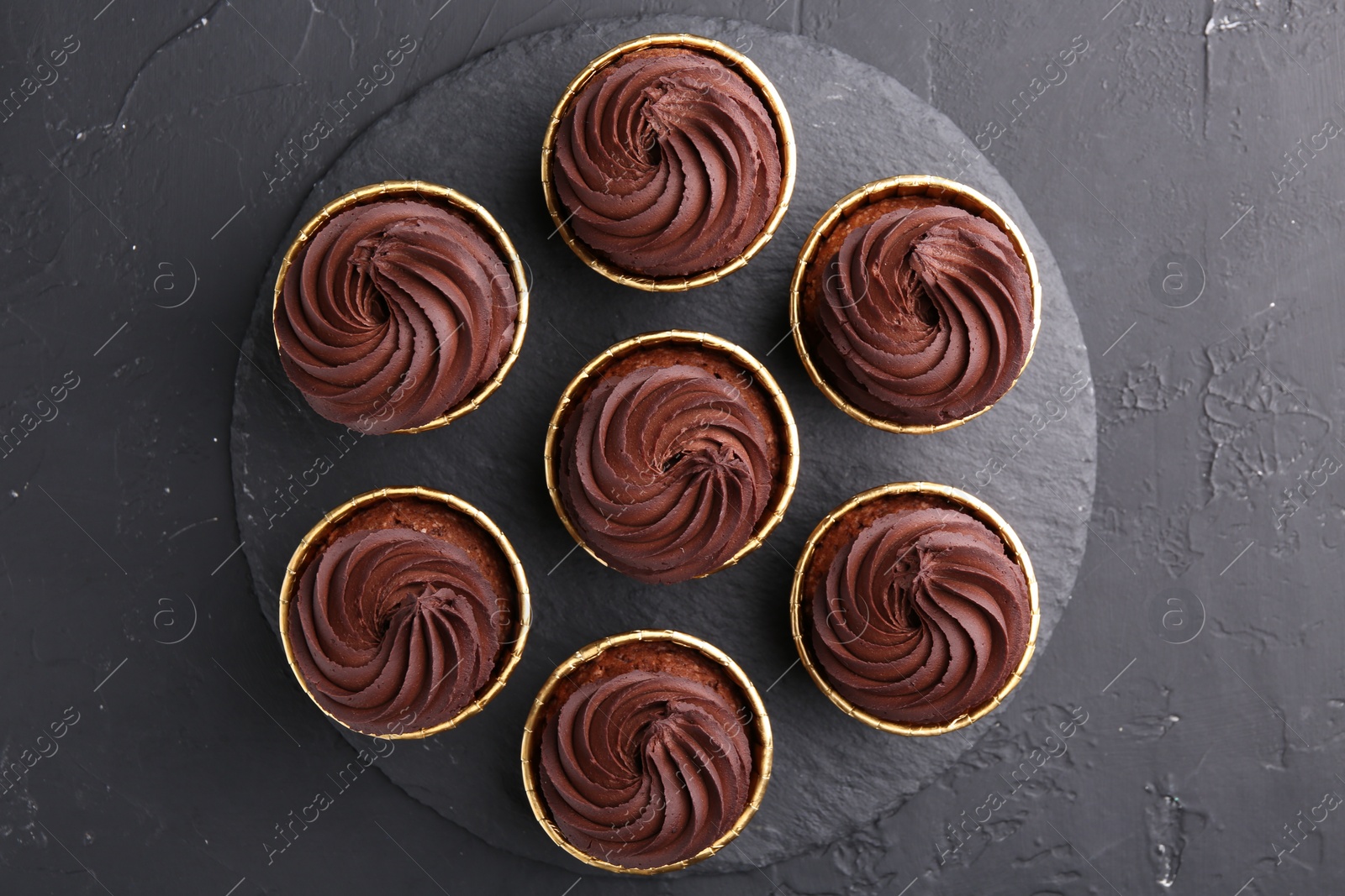 Photo of Delicious chocolate cupcakes on black textured table, top view