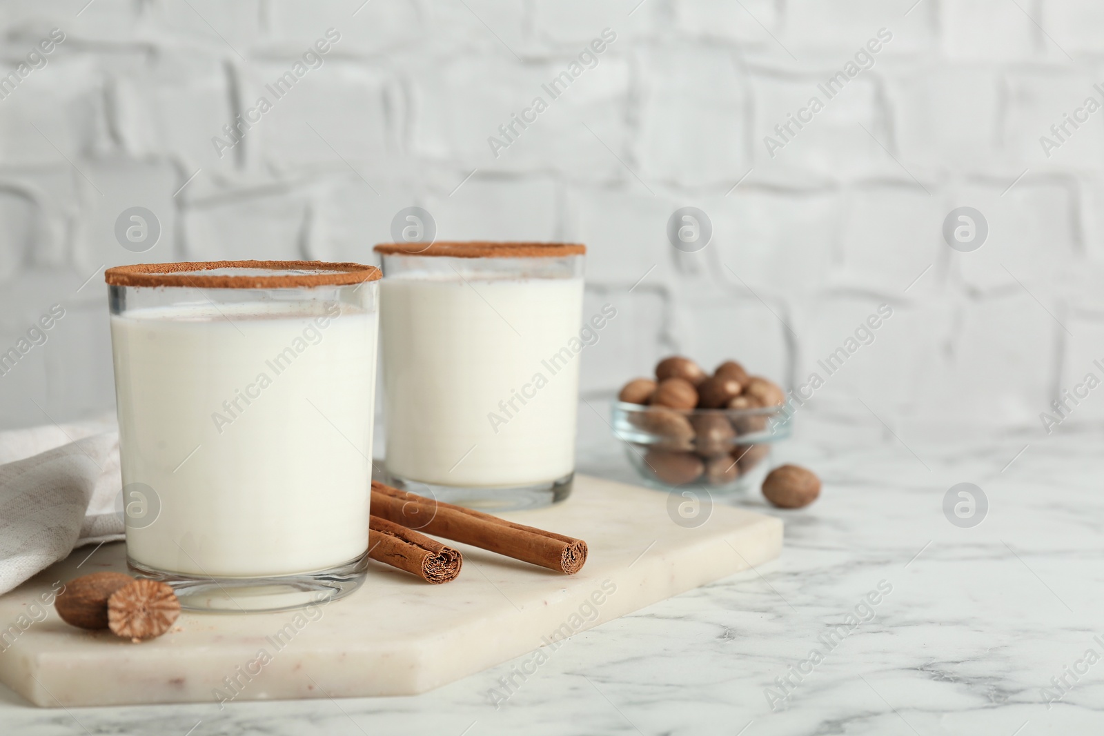 Photo of Glasses of milk with nutmeg on white marble table. Space for text