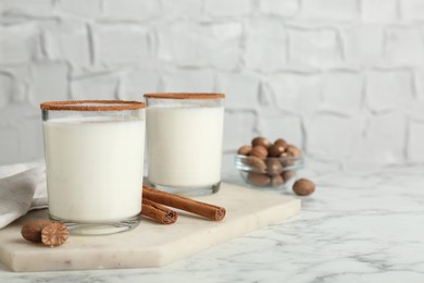 Glasses of milk with nutmeg on white marble table. Space for text